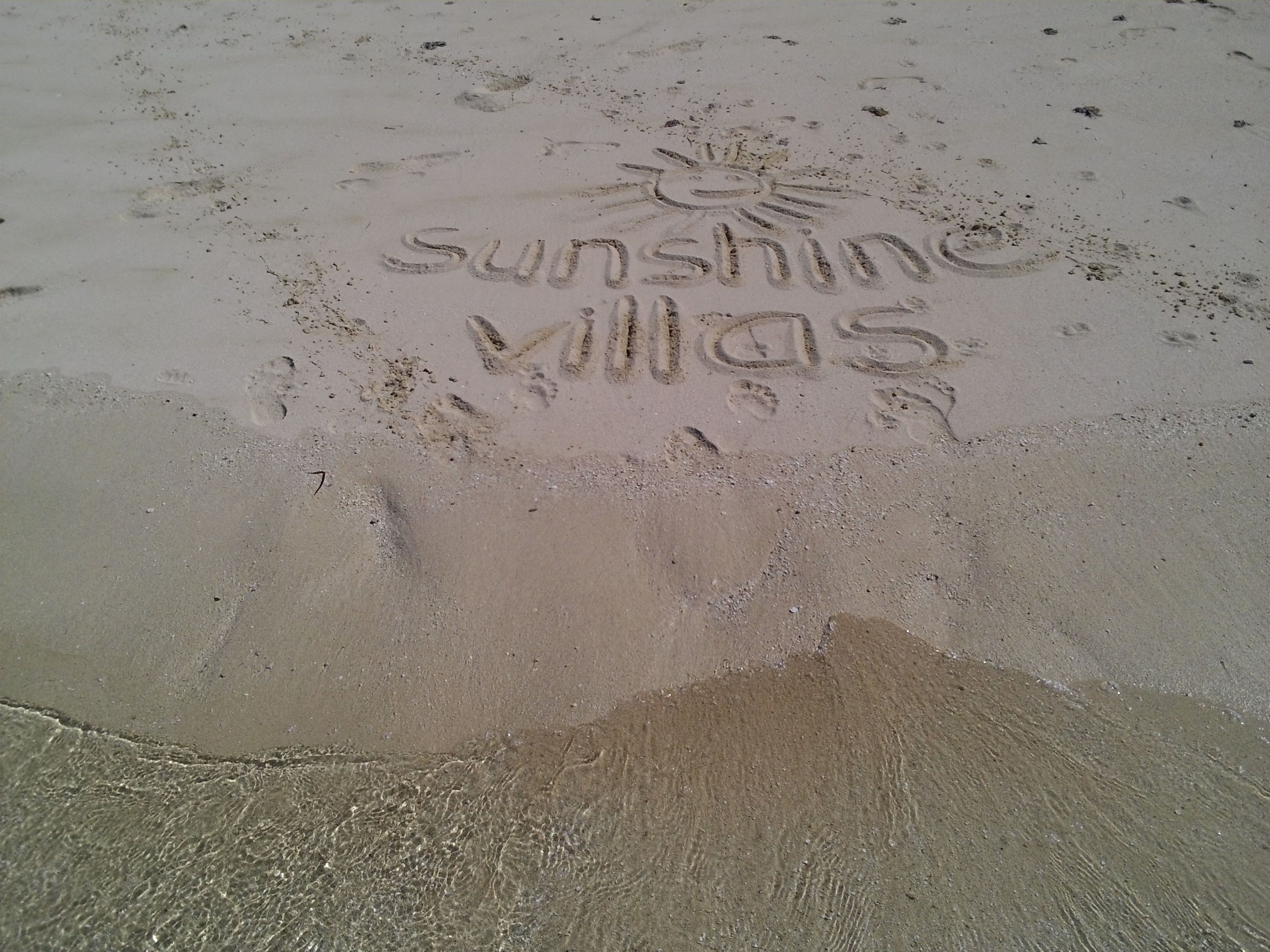 A sandy beach with footprints and the words "sunshine Villas" etched into the sand.