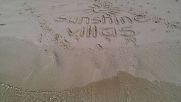 A sandy beach with footprints and the words "sunshine Villas" etched into the sand.