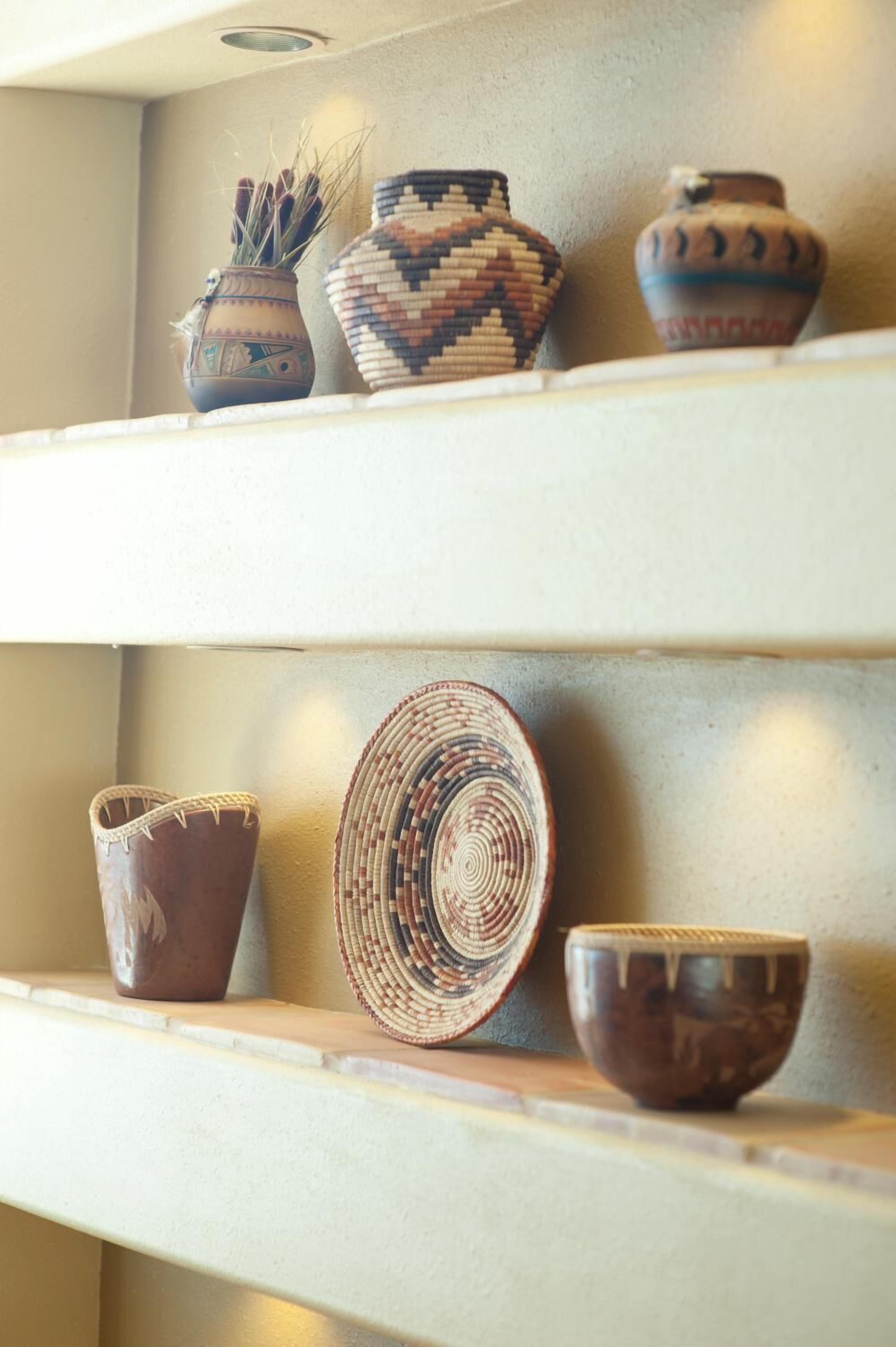 A shelf with various pottery items including a woven basket, a bowl, and a vase.