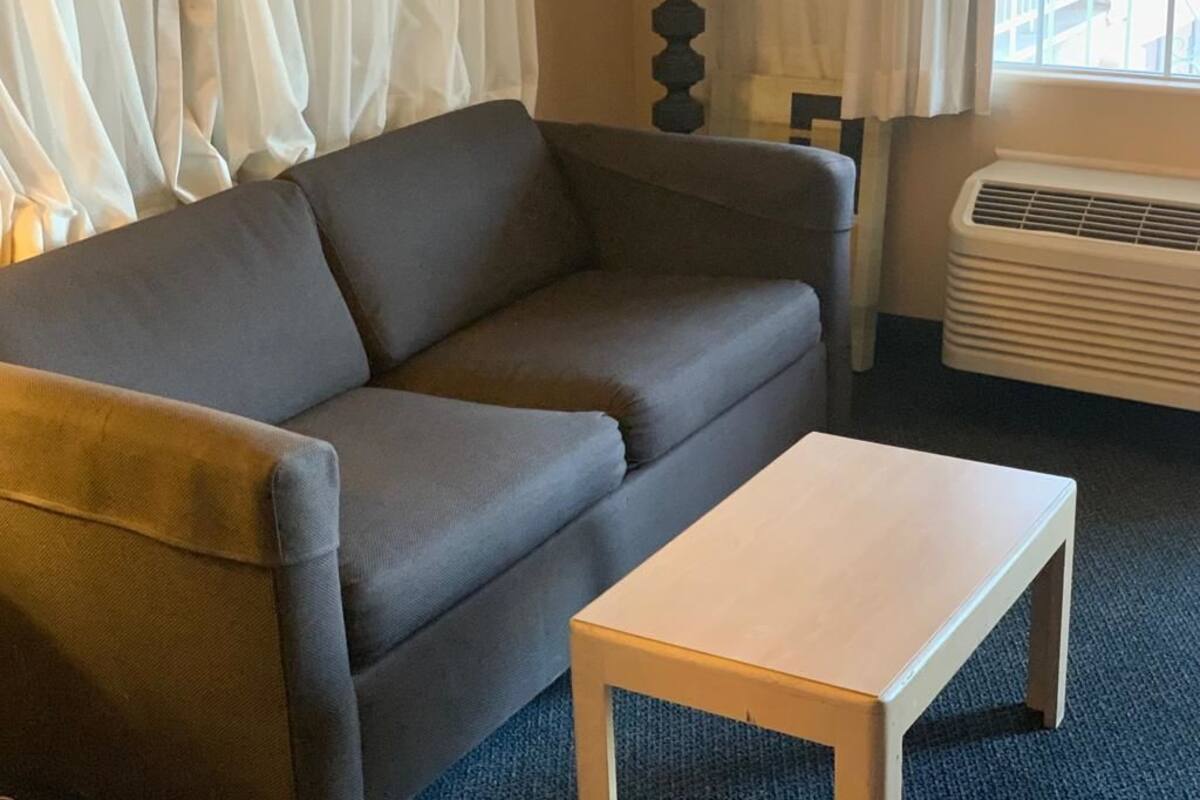 A grey sofa and a small wooden table in a room with a window and an air conditioner.