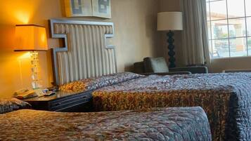 A hotel room with two beds, a nightstand with a lamp, a wall-mounted TV, and a window with curtains.