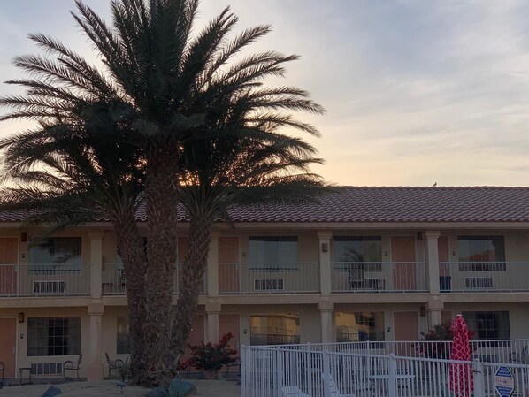 A two-story building with balconies, a palm tree, and a fenced patio area.