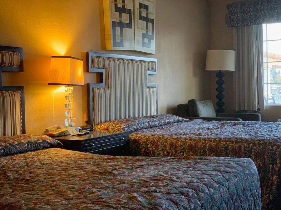 A hotel room with two beds, a desk with a lamp, a telephone, and a chair.