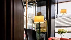 Una sala moderna con un sofá rojo, un sillón oscuro y un reposapiés azul. Hay dos lámparas de pie y un jarrón con flores sobre una mesa.
