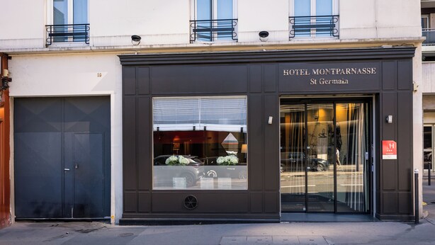 Fachada de un hotel con entrada oscura, ventanas grandes y un cartel que dice "HOTEL MONTPARNASSE St Germain".