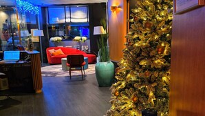 Un vestíbulo de hotel con un árbol de Navidad, asientos rojos, un florero verde y una escultura de madera.