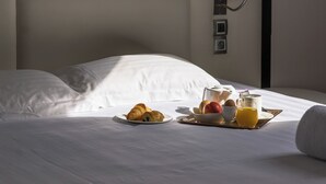 Una cama bien tendida con sábanas blancas, una bandeja de desayuno con cruasanes, fruta y jugo, y un cabecero moderno con diseño minimalista.