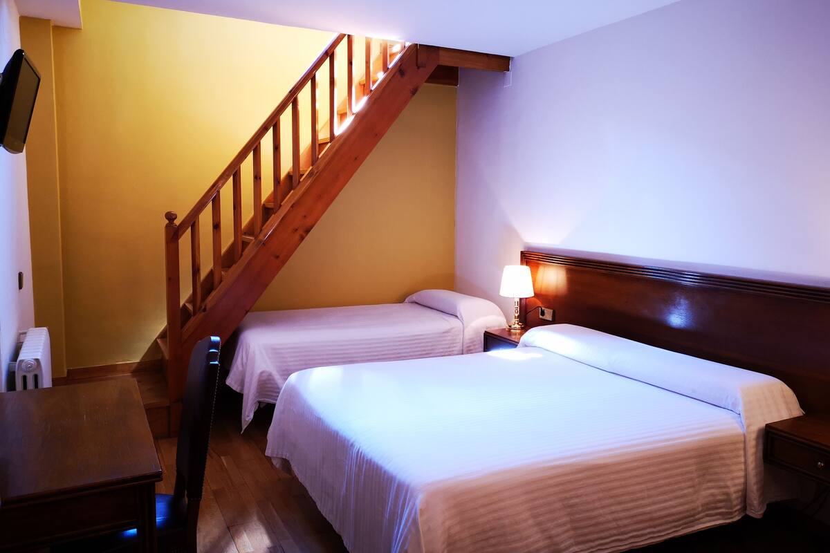 Hotellihuone, jossa on kaksi erillistä sänkyä, puinen portaikko, yöpöytä lampun kanssa ja patteri.