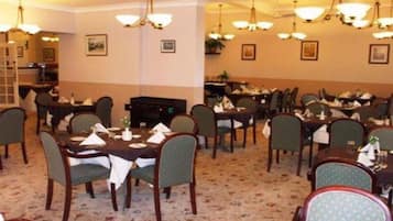 A dining area with multiple tables and chairs, chandeliers, and framed pictures on the walls.
