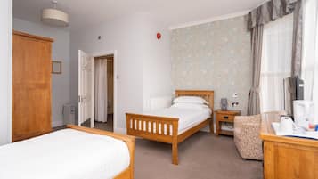 A hotel room with two wooden beds, a small bedside table with a lamp, a chair, and a television.