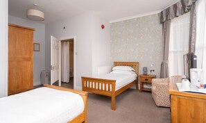 A hotel room with two wooden beds, a small bedside table with a lamp, a chair, and a television.