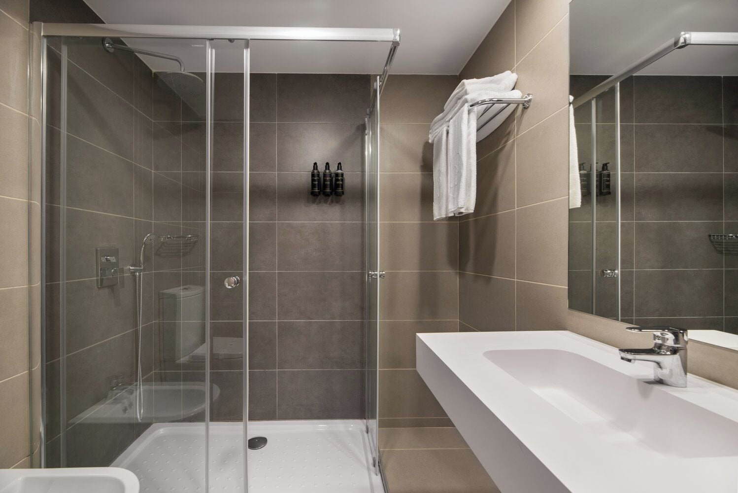 A modern bathroom with a glass-enclosed shower, a white sink, and a large mirror.