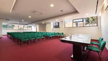 Un salón de conferencias con filas de sillas verdes, una mesa grande y ventanas amplias.