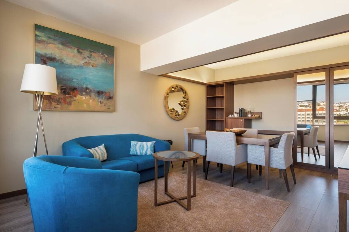 A modern living room with a blue sofa, a coffee table, and a dining area with chairs and a table.