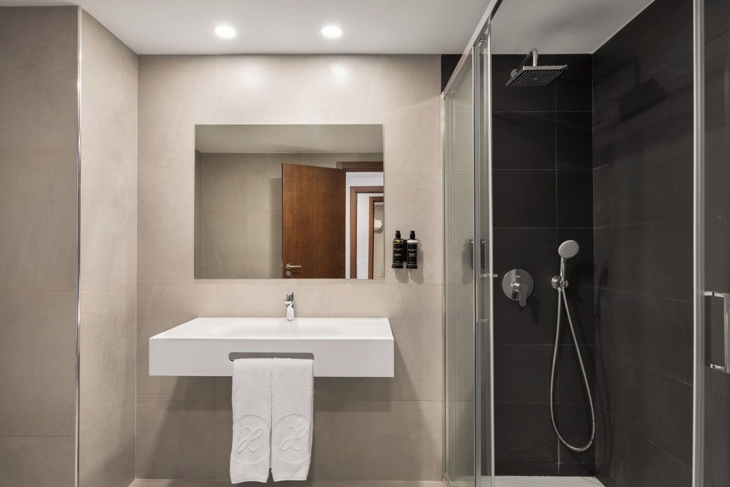 Une salle de bain moderne avec un lavabo blanc, un grand miroir, une douche en verre et une serviette accrochée au mur.