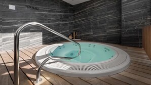Un jacuzzi moderno en el interior con una terraza de madera, frente a paredes de mármol oscuro.