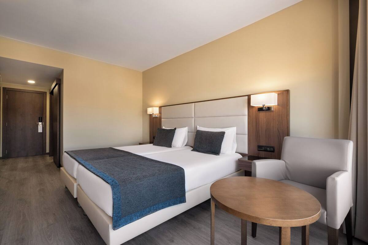 A hotel room with a large bed, a bedside table, a chair, and a small table.