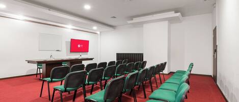 Uma sala de conferências com uma mesa comprida, fileiras de cadeiras, uma tela de projetor e uma lousa.