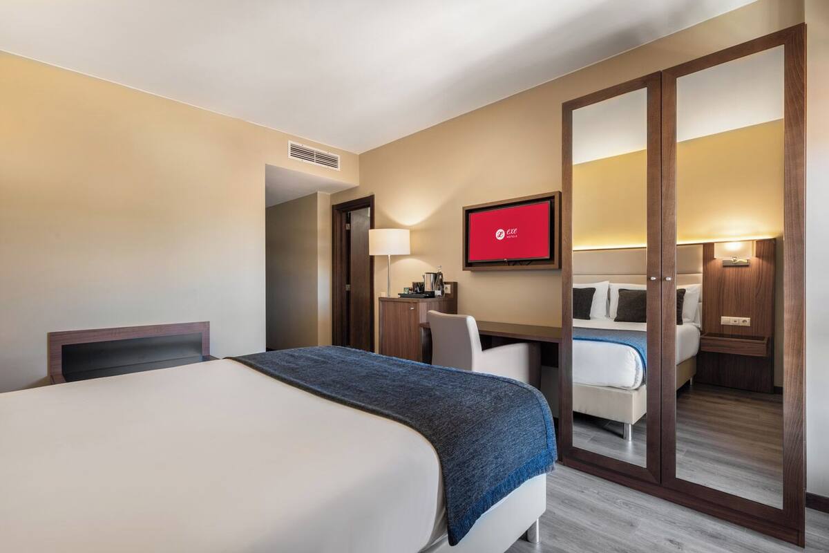 A hotel room with a bed, a desk, a chair, a TV, and a wardrobe.