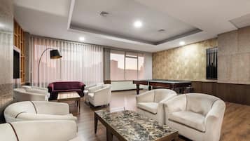 A modern lounge area with a pool table, comfortable seating, and a large window offering a city view.