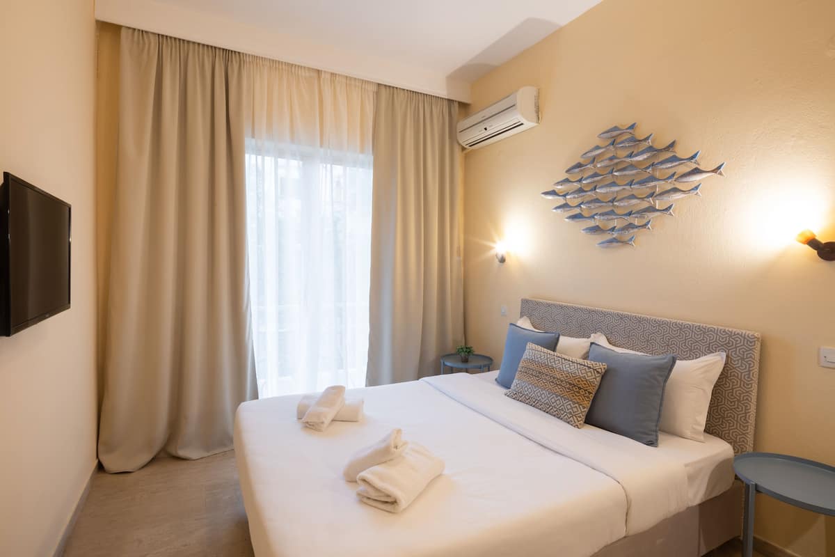 A hotel room with a bed, curtains, a wall-mounted air conditioner, a wall decoration of fish, and a small table.