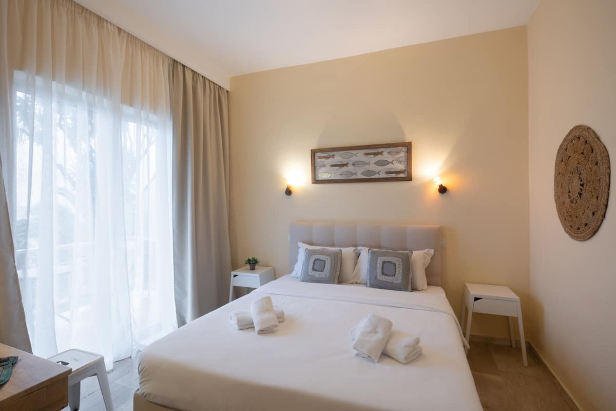 A hotel room with a large bed, two bedside tables, a wall-mounted light fixture, and a decorative wall hanging.