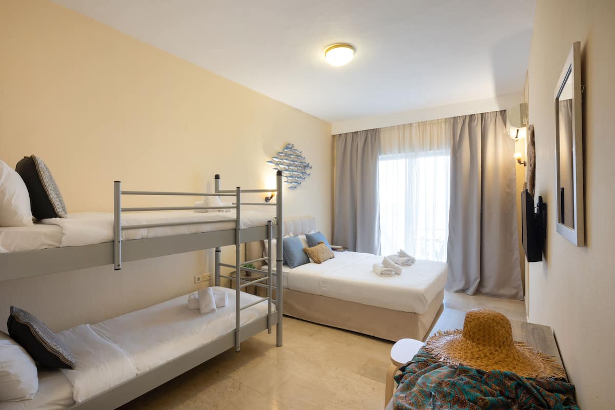 A hotel room with bunk beds, a single bed, a small table, and a large window with curtains.