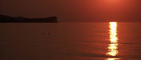 A sunset over a calm body of water with a silhouette of a landmass in the distance.