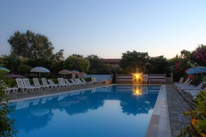 A swimming pool with lounge chairs and umbrellas, surrounded by trees and a building in the background. - Nireas Resort Corfu (Corfu)