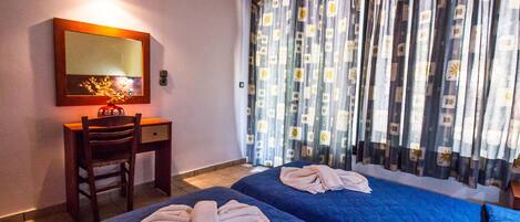 Hotelkamer met twee bedden, een bureau, een stoel, een spiegel en een raam met patroon gordijnen.