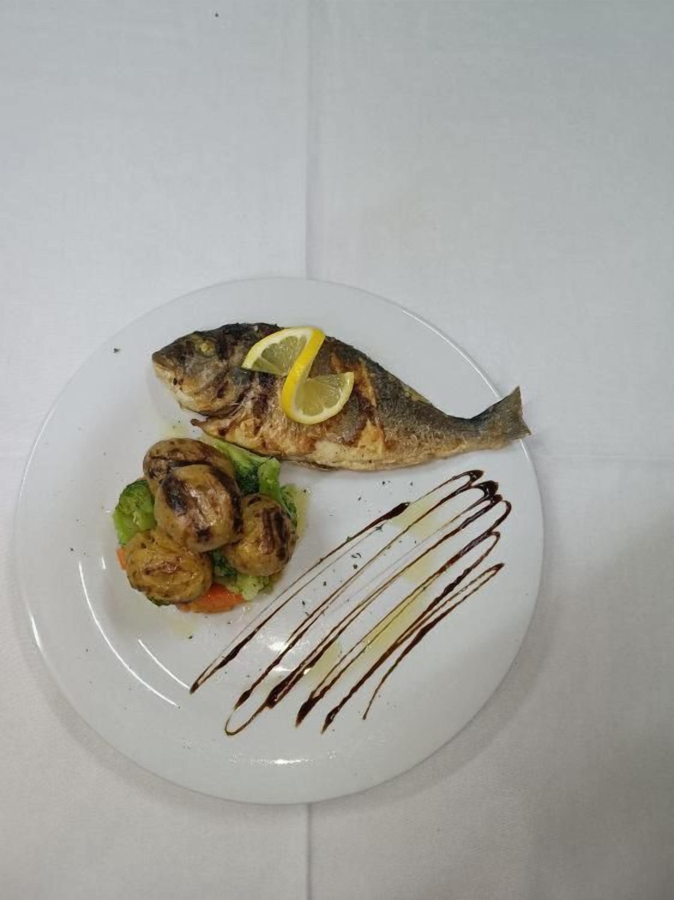 A plate with grilled fish, vegetables, and a lemon slice.
