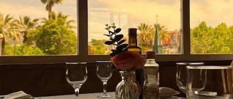 Mesa lista para comer con vistas a palmeras y al atardecer a través de amplios ventanales.