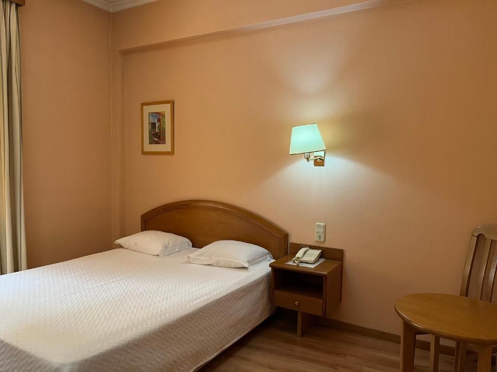 A hotel room with a bed, a nightstand, a lamp, a chair, and a picture on the wall.