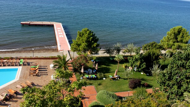 A poolside area with lounge chairs and umbrellas, a grassy lawn, and a view of the sea. - Hotel Rena (Ayvacik)
