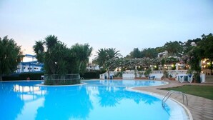 Ein Pool mit gepflastertem Deck, umgeben von Palmen und einem Gebäude mit weißem Zaun.