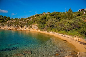 A coastal landscape with a clear beach, rocky outcrops, and dense greenery. - Thalassokipos (Sithonia)
