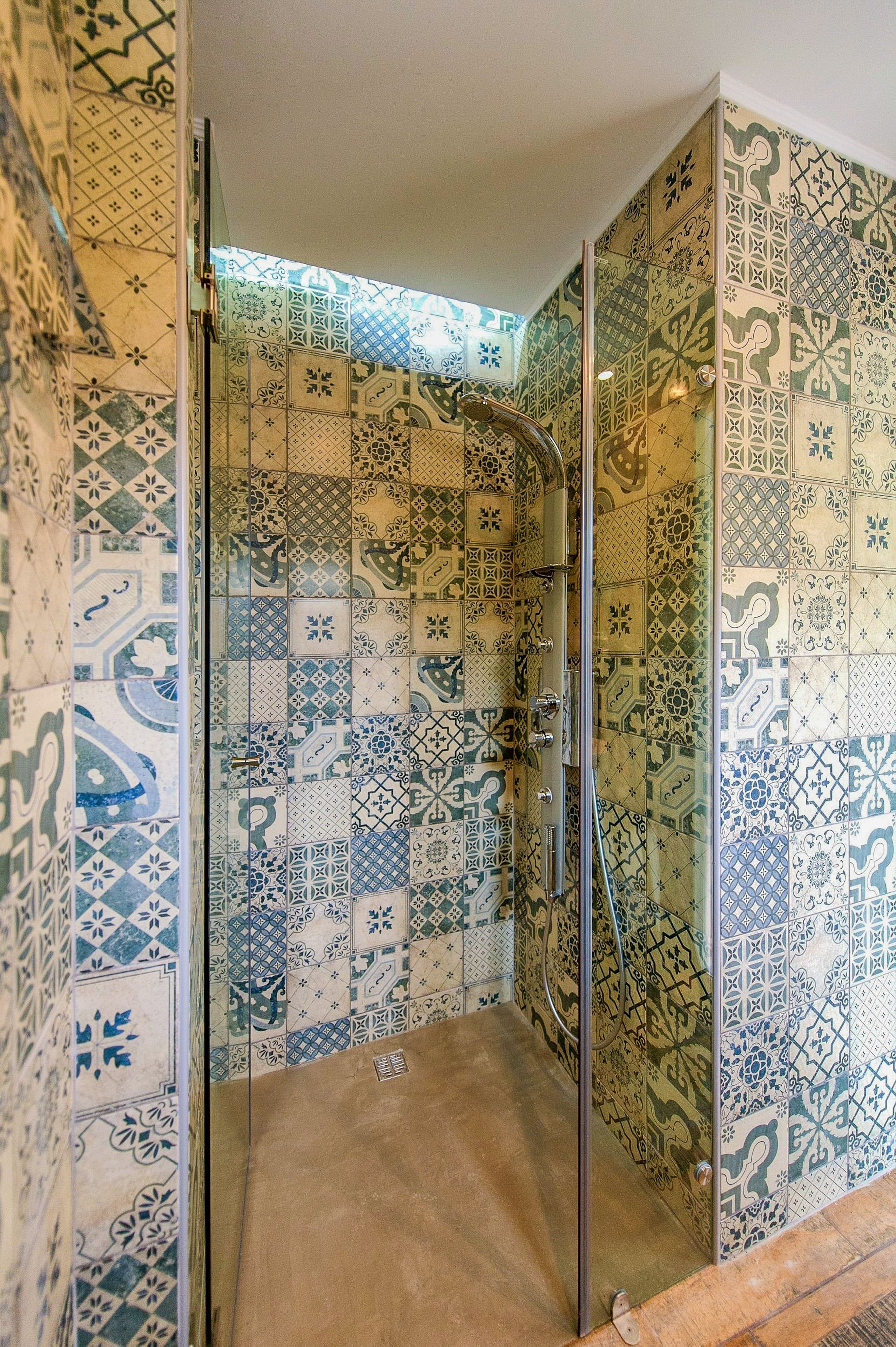 Ducha con puerta de vidrio y paredes cubiertas de azulejos con diseño.