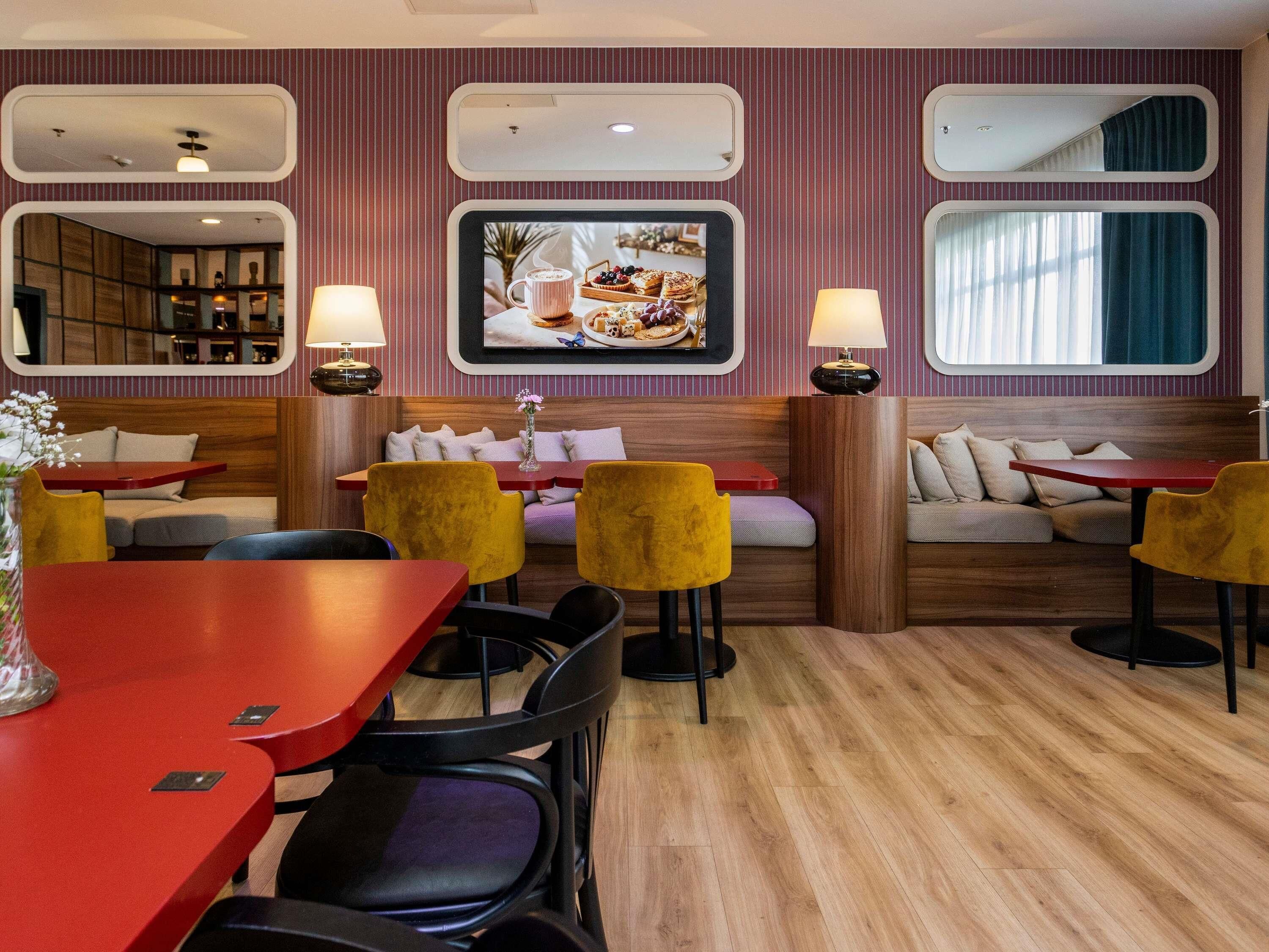 A modern interior with a seating area featuring yellow chairs, a wooden table, and a television displaying food.