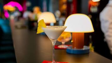 A martini glass with a yellow fruit garnish on a red napkin, placed on a bar counter with a lit lamp in the background.