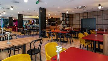 Een modern restaurant met verschillende eetgedeeltes, waaronder een bar en een zithoek met een open haard.