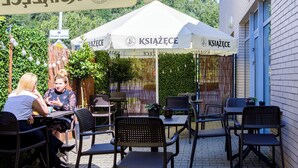 Un café al aire libre con mesas y sillas, rodeado de follaje y una valla.