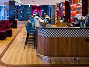 A bar area with a checkered counter, bar stools, and a neon-lit archway in the background. - ibis Styles Walbrzych (Walbrzych)