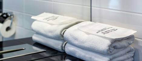 A stack of folded towels with a label on top, placed on a black surface with a metallic towel rack in a bathroom setting.