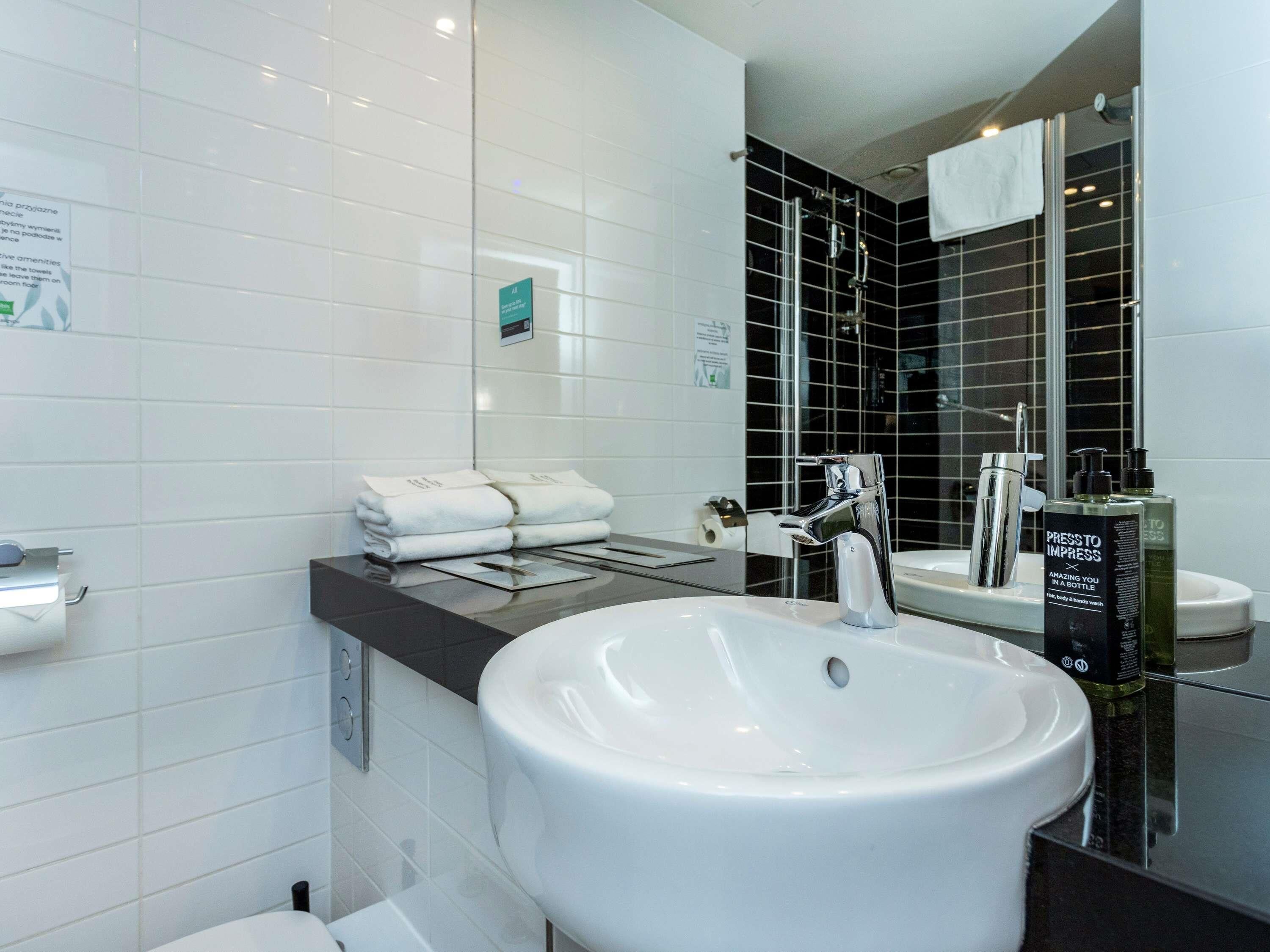 Un baño moderno con un lavamanos blanco grande, un espejo y una zona de ducha con azulejos negros.