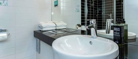 Un baño moderno con un lavamanos blanco grande, un espejo y una zona de ducha con azulejos negros.
