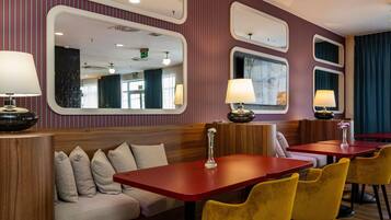 A hotel room with a wooden headboard, a sofa with cushions, a red table, yellow chairs, and wall-mounted lamps.