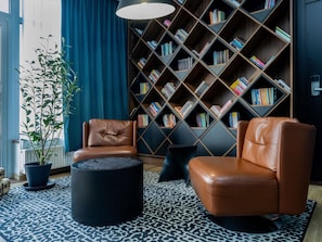 Una sala moderna con sillones de cuero, un otoman negro redondo, un tapete estampado y una estantería llena de libros.