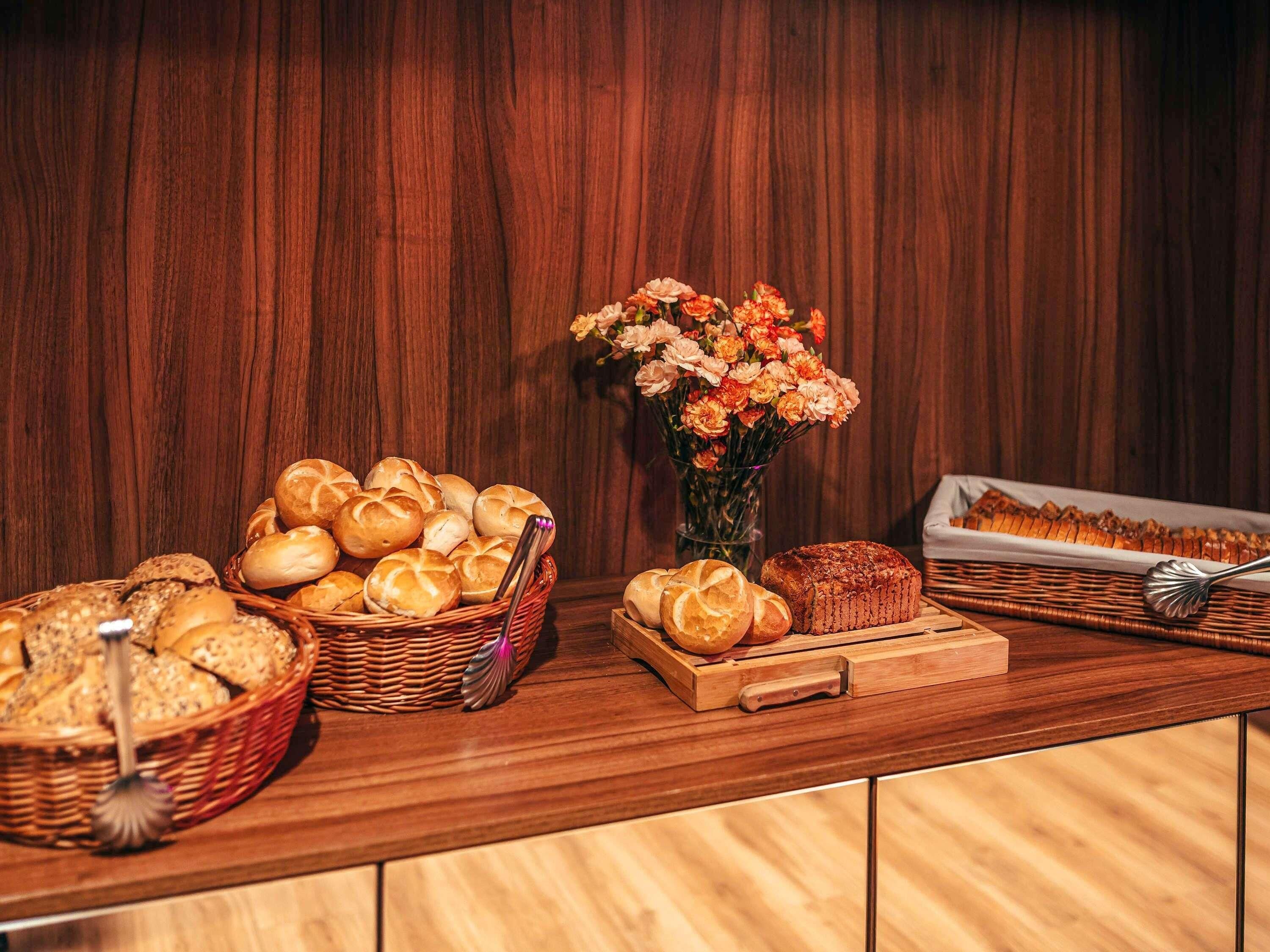 A buffet table with various breads and pastries, a vase of flowers, and a wooden backdrop.