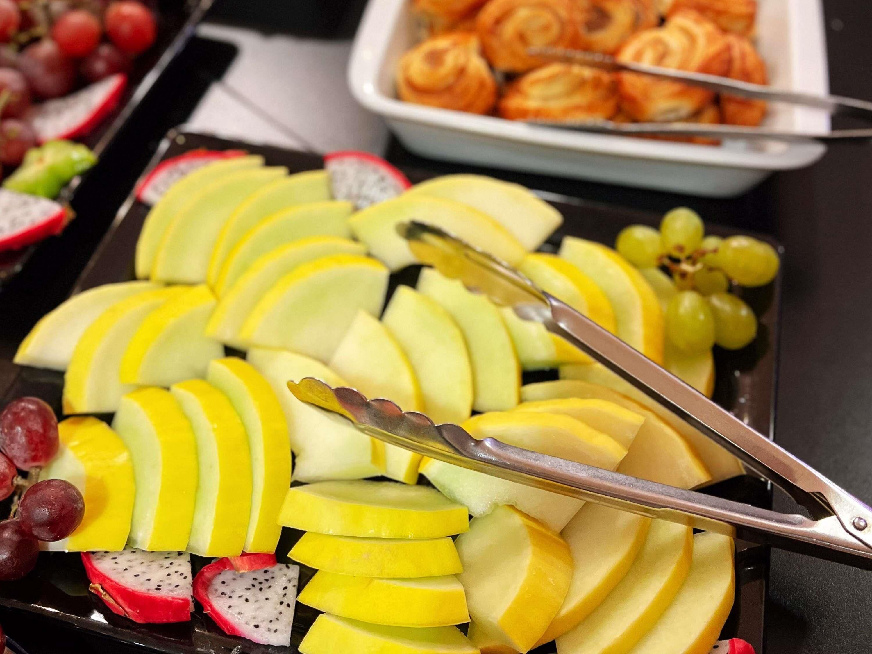 A fruit platter with tongs, grapes, and dragon fruit slices.