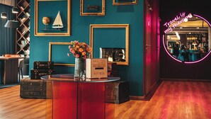 A reception desk with a 'Welcome' sign, a keybox, and a vase of flowers. There are framed pictures on the wall, a neon sign, and a wooden floor. - ibis Styles Walbrzych (Walbrzych)